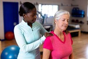 Female physiotherapist giving back massage to active senior woman in sports center