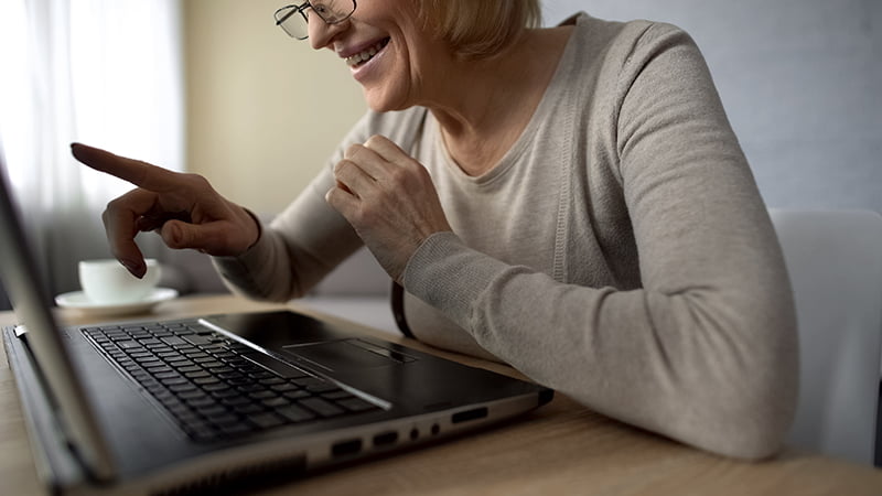 Senior lady delighted to talk to children in internet, looking at laptop screen