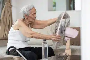 Overheated asian senior woman sweating,high temperature in sunny day while stay at home,cooling herself in front of an electric fan,old elderly suffering from heat.