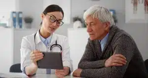 Young female doctor talking to aged male patient and holding digital tablet. Medical specialist showing senior patient test results on tablet pc in clinic office