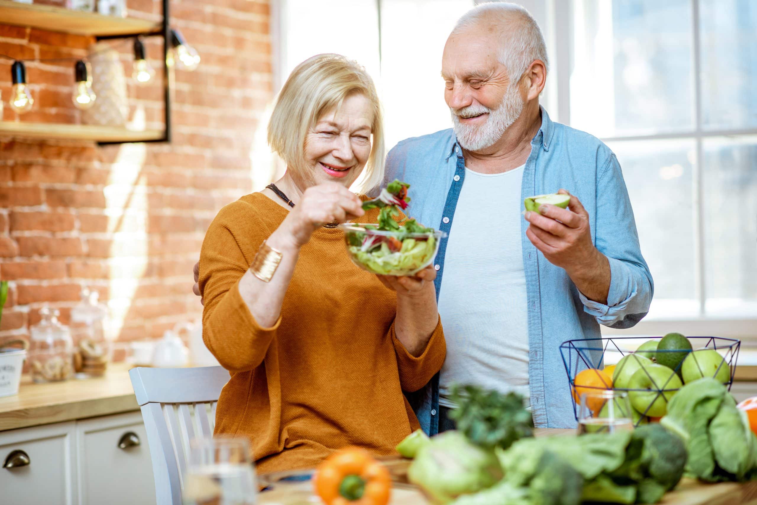 Portrait of a cheerful senior couple with salad and healthy food on the kitchen at home. Concept of healthy nutrition in older age