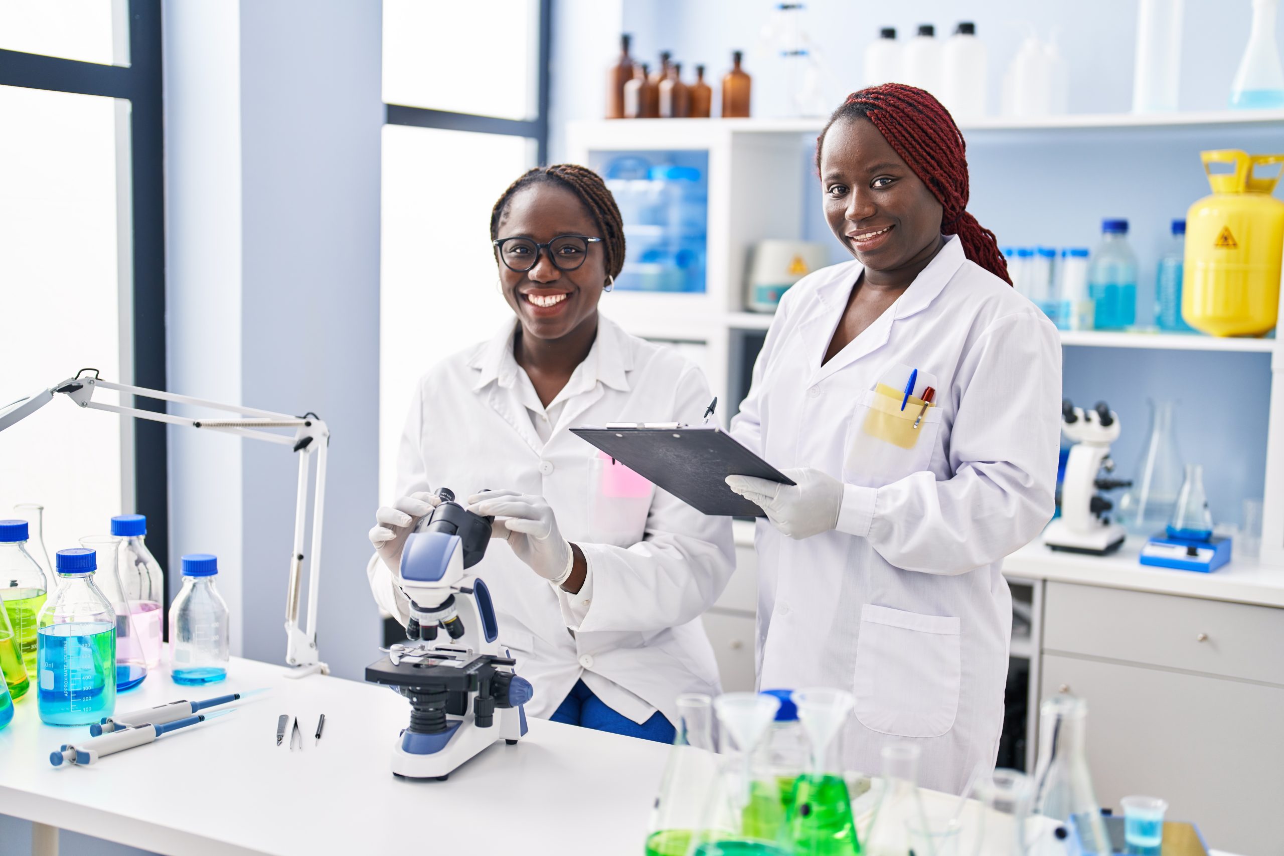 African american women scientists using microscope writing on document at laboratory