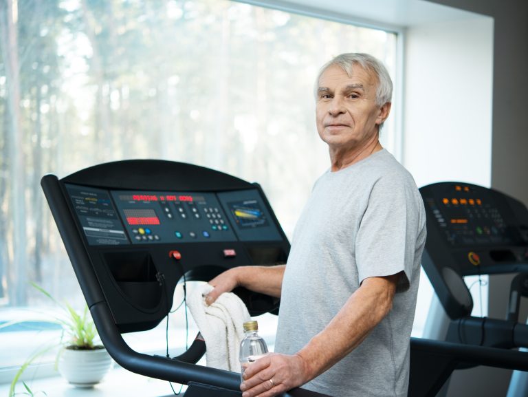 Tired senior man on a treadmill with towel and bottle of water