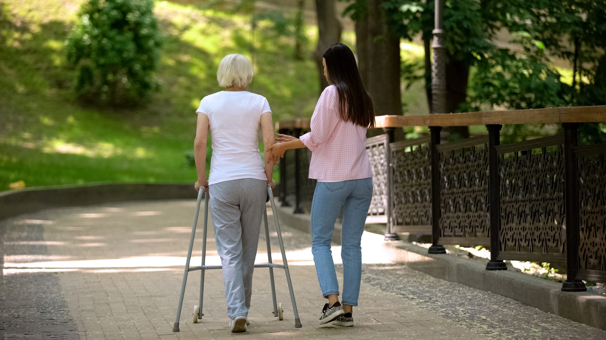 walking with elderly woman using walker in hospital park, disability