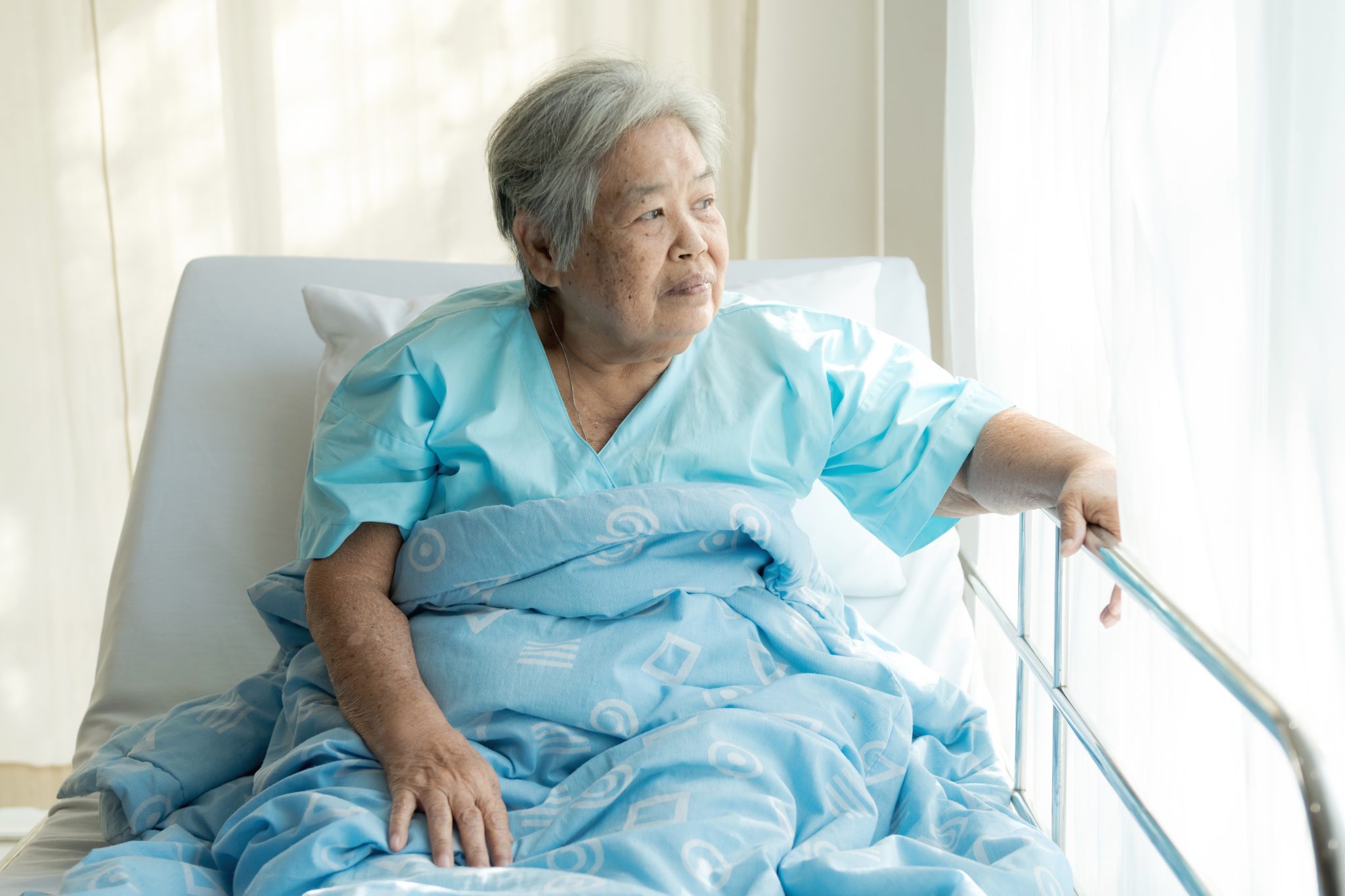 Elderly patient alone in bed. Alone and stress, missing her grand children. Looking at window. Very senior, old chinese woman.