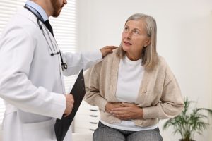 Doctor consulting senior patient with stomach pain in clinic, closeup
