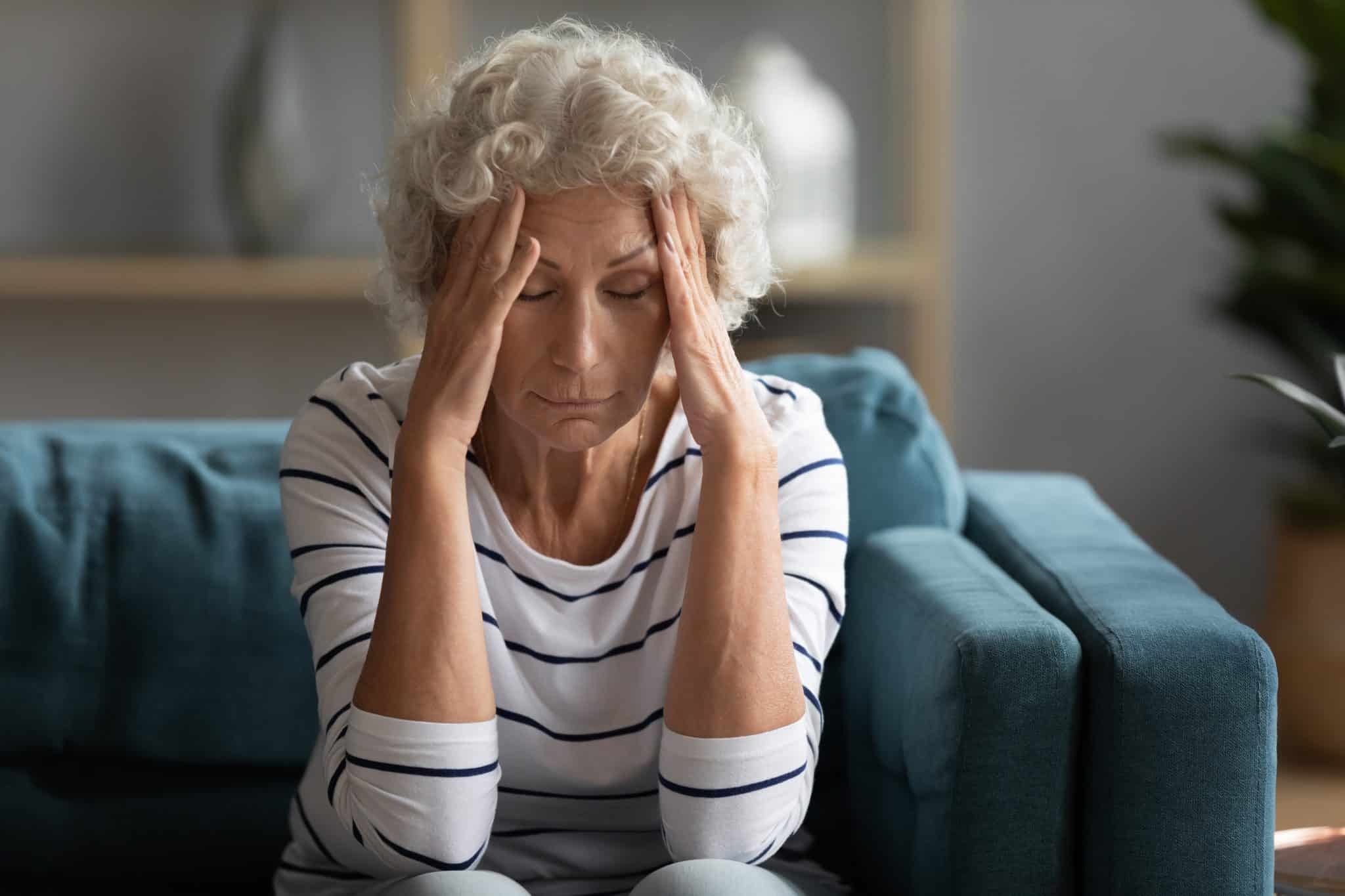 Unhealthy middle aged senior stressed woman holding head in hands, having painful feelings alone at home. Unhappy older mature granny suffering from headache migraine dizziness high blood pressure.